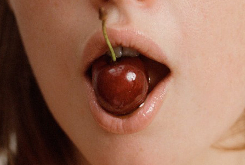 Qu'est-ce qu'un fantasme sexuel ? image de bouche tenant une cerise rouge foncé de façon sensuelle avec ses lèvres et ses dents